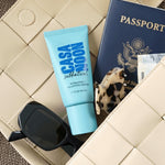 Blue tube of 'Casa Noon' product, sunglasses, and a passport on a textured surface