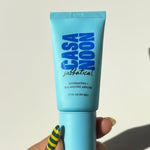 Casa Noon skincare product tube held by a hand with green and yellow striped nail polish on a white background.