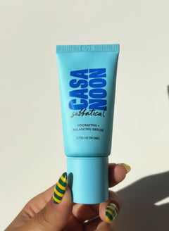 Casa Noon skincare product tube held by a hand with green and yellow striped nail polish on a white background.