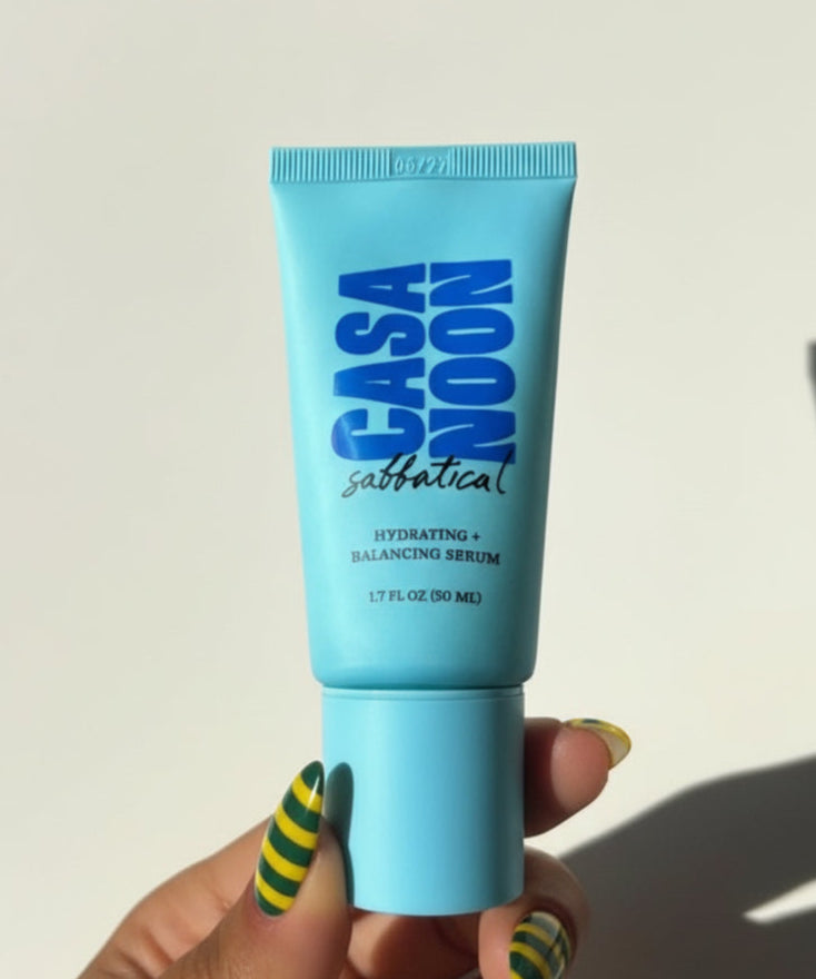 Casa Noon skincare product tube held by a hand with green and yellow striped nail polish on a white background.