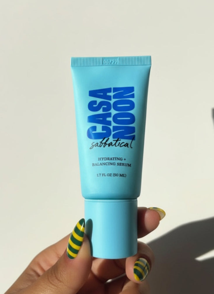 Casa Noon skincare product tube held by a hand with green and yellow striped nail polish on a white background.